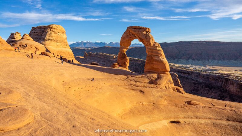 Photo of a natural sandstone arch behind a sloping hole in the landscape under a clear blue sky