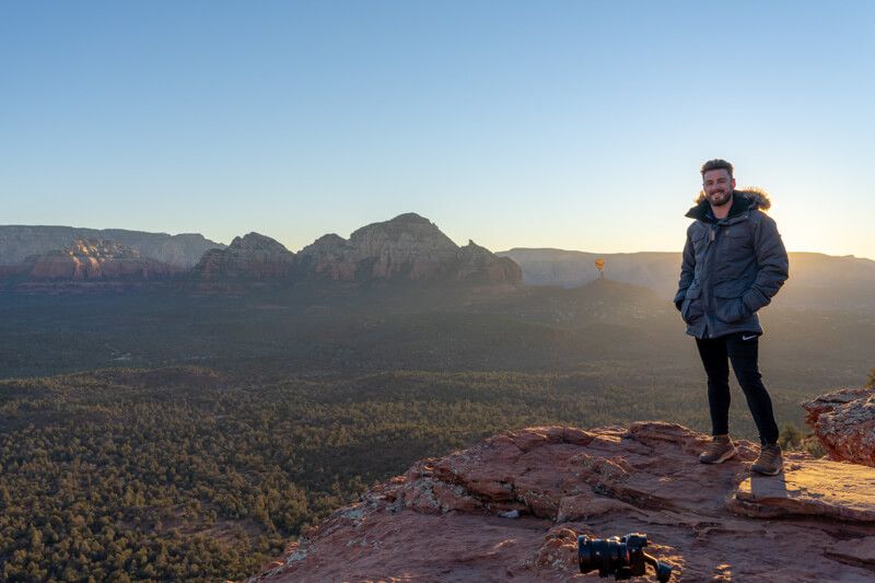 Photo of Mark Morgan in a winter coat at sunrise on top of a mesa with far reaching views over Sedona AZ