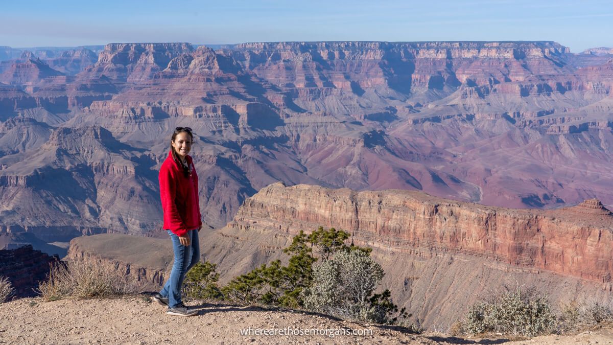 Tourist standing on a rocky ledge at a Grand Canyon viewpoint overlooking the canyon on a sunny day