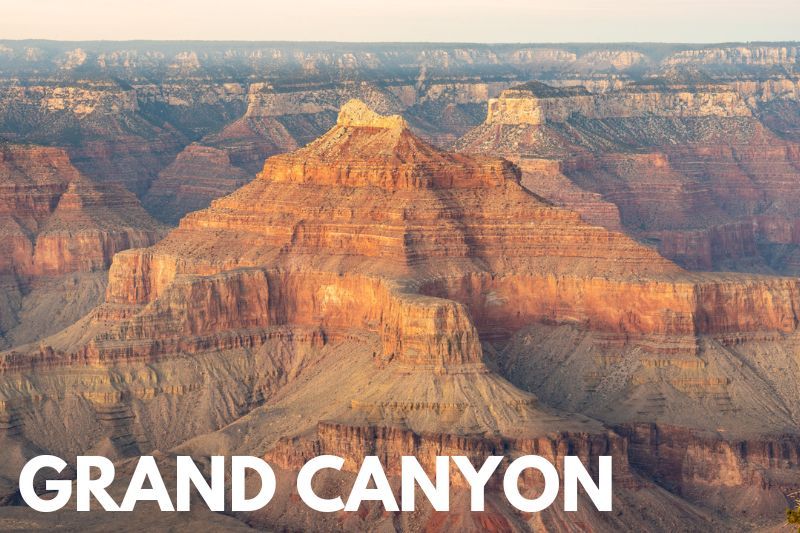 Photo of sandstone formations as far as the eye can see lightly glowing a deep orange color at dawn with text reading Grand Canyon