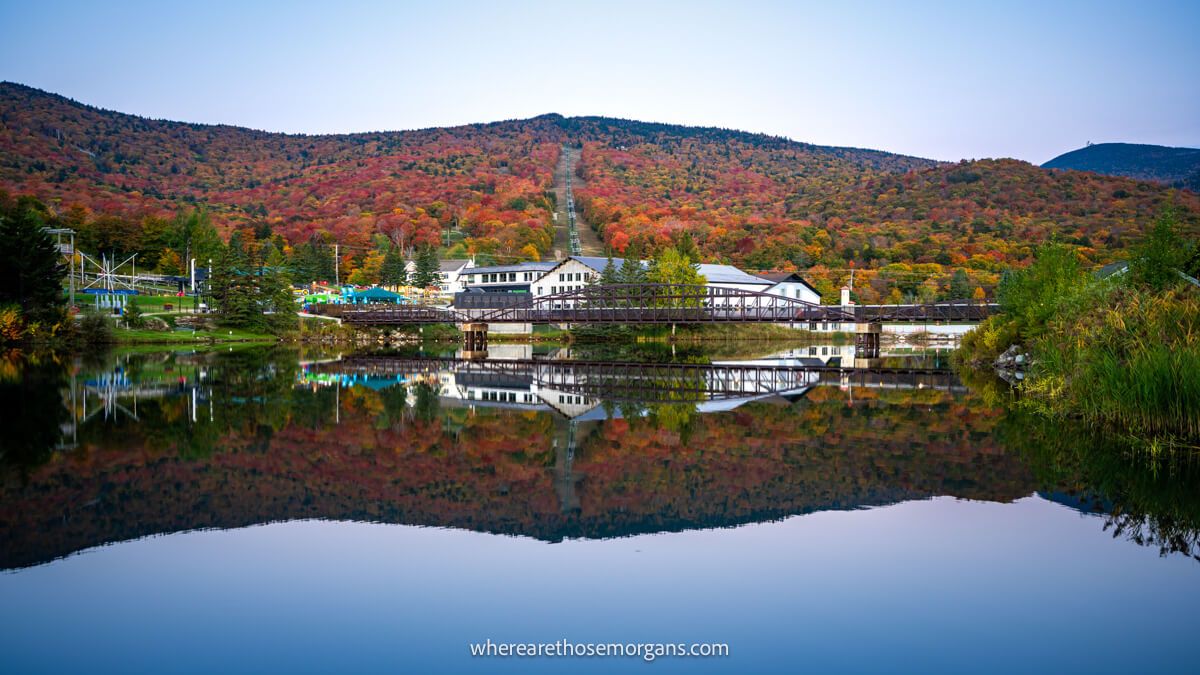 White building and rolling hills covered in colorful tree leaves reflecting perfectly in a still lake at dawn