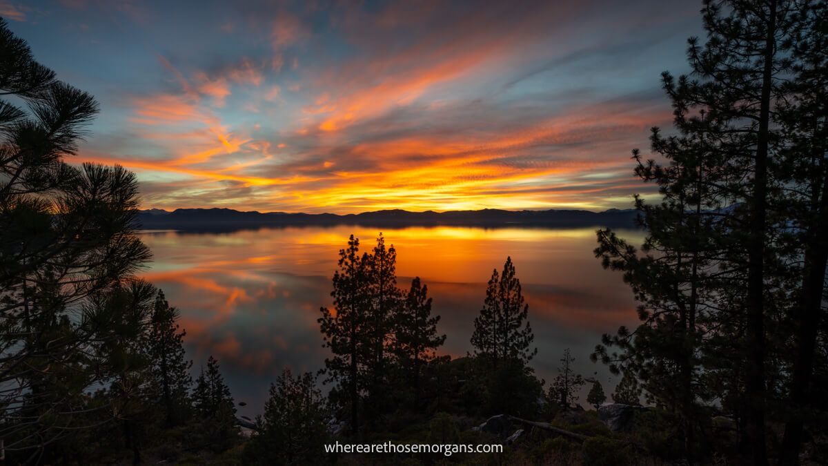 Huge lake behind silhouetted trees with clouds in the sky being lit up by sunset colors at a stunning Lake Tahoe photo spot