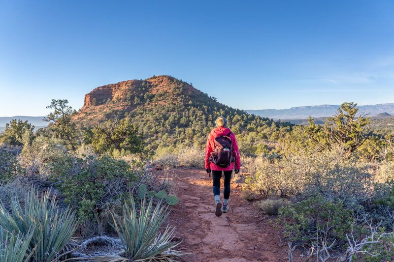 Photo of Kristen Morgan hiking a trail in Sedona at dawn with winter clothes under a clear blue sky