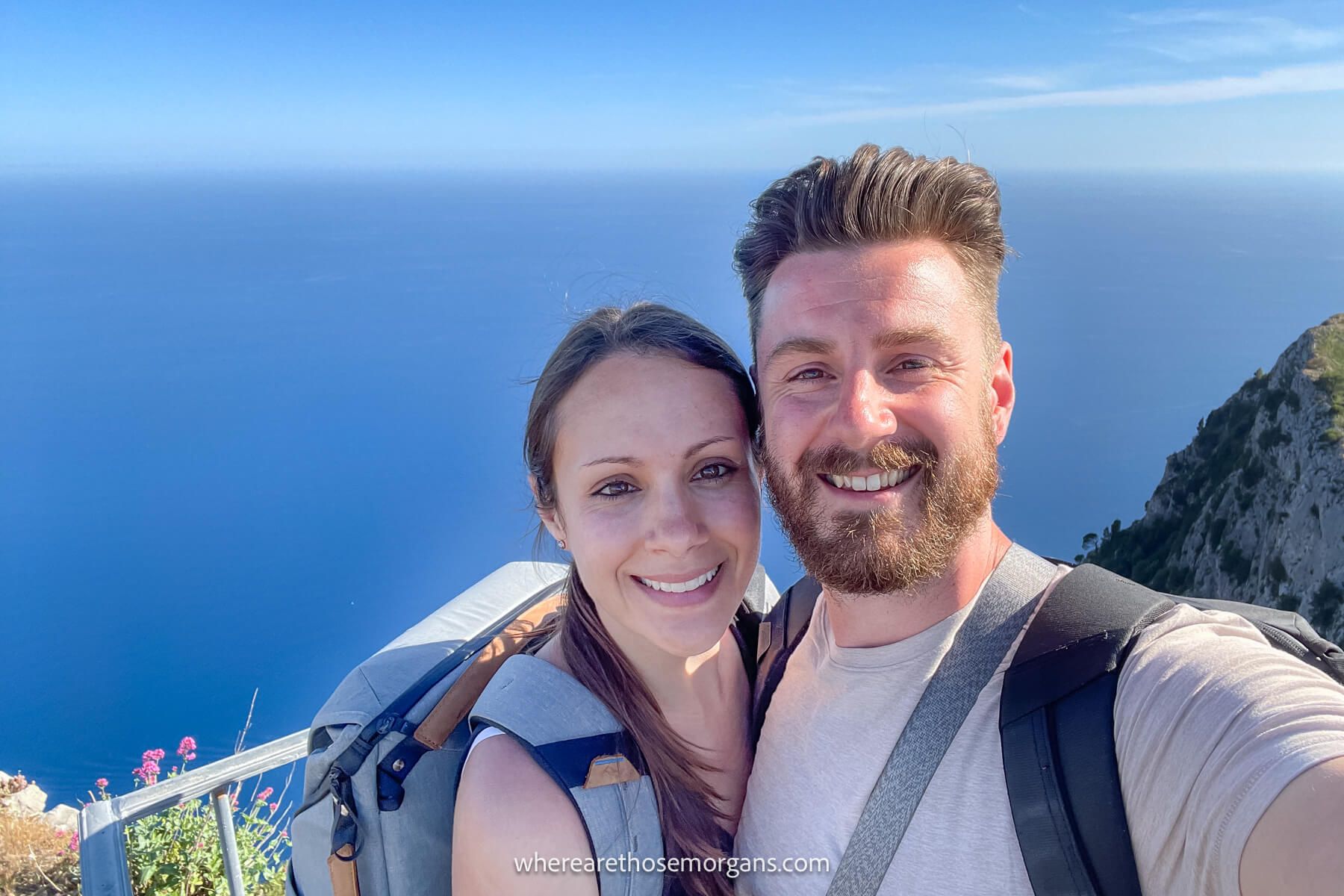 Photo of Mark and Kristen Morgan from Where Are Those Morgans taking a selfie from a cliffside walk with views over the ocean in Italy