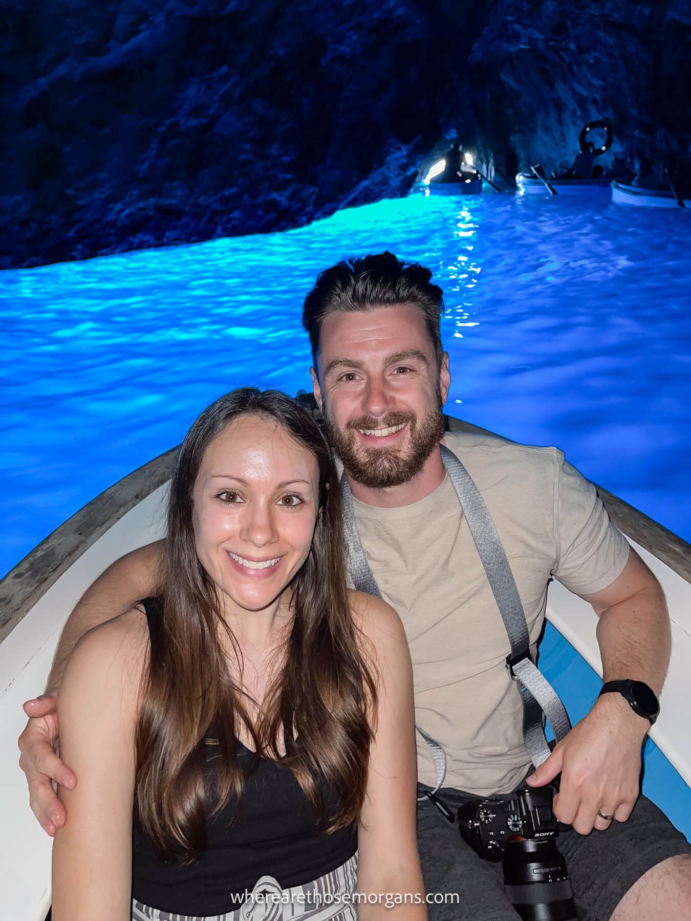 Photo of Mark and Kristen Morgan from Where Are Those Morgans sitting closely together in a small boat floating on deep blue colored water inside a cave in Capri, Italy