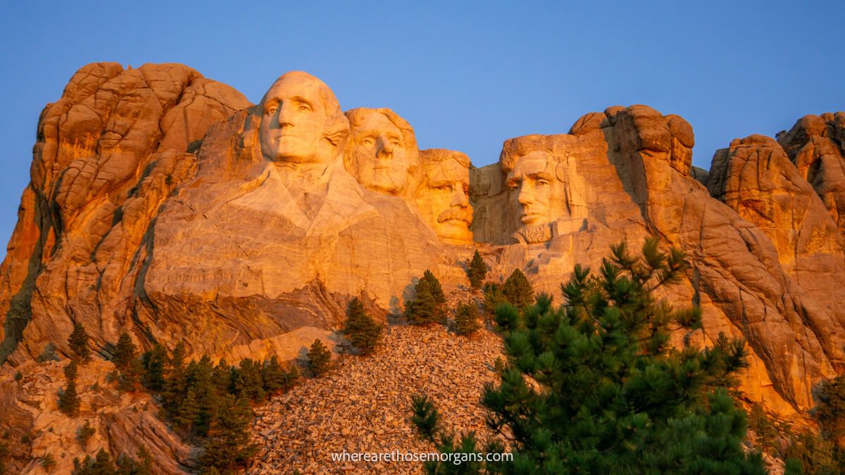 Photo of the Mount Rushmore sculpture glowing orange at sunrise against a clear blue sky