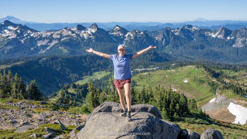 Photo of a hiker standing on a rock with arms stretched out and far reaching views over mountain peak behind