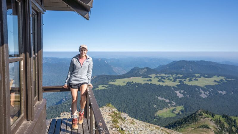 Photo of a hiker sat on a wooden fence in a fire tower with sweeping views over a rural mountainous landscape