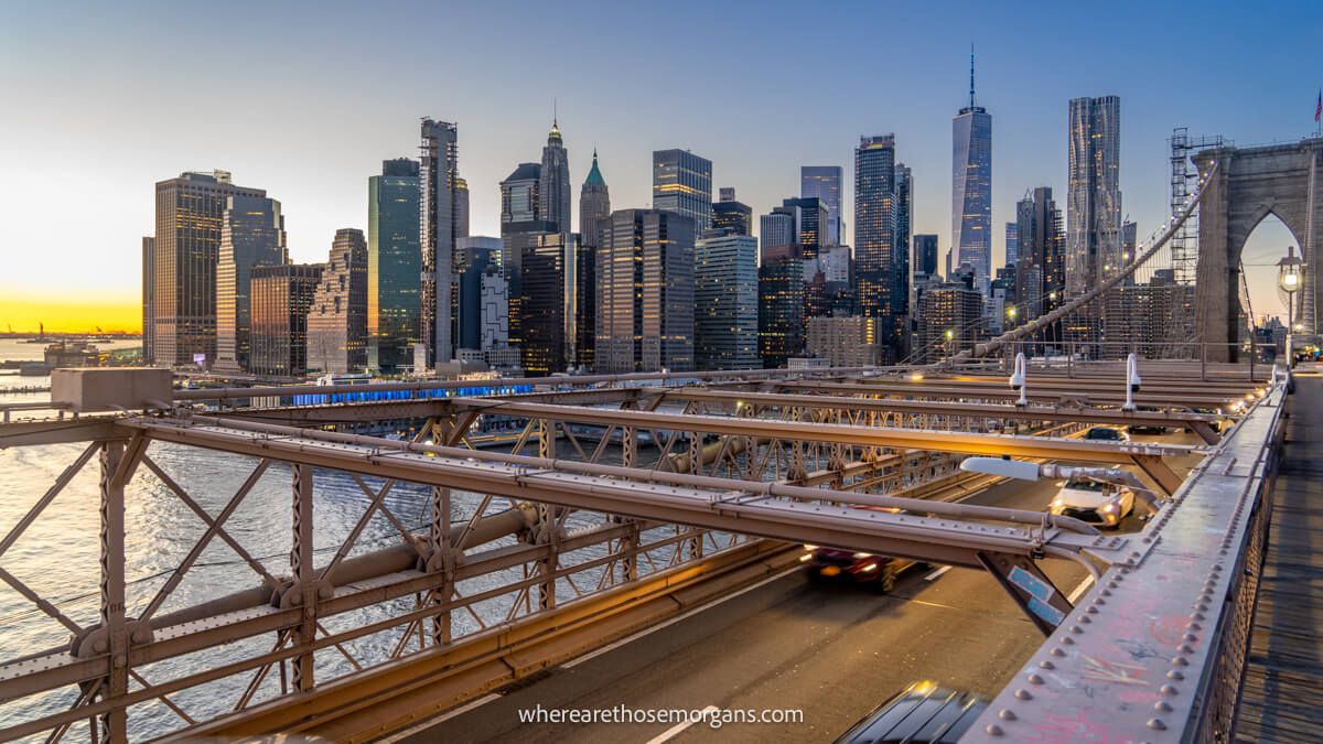 The New York City skyline at sunset behind cars crossing the Brooklyn Bridge