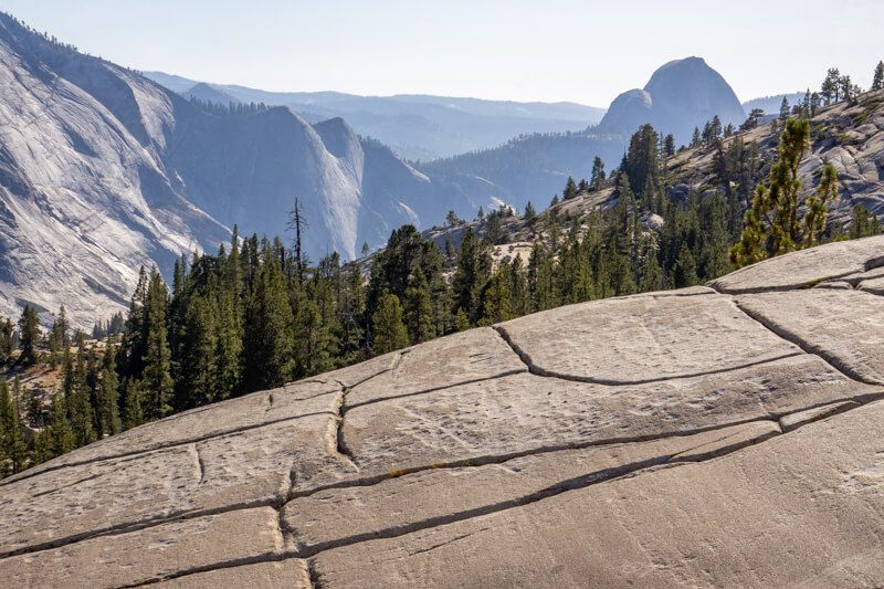 Photo of a cracked rock face with trees and views leading to distant granite mountains on a hazy day