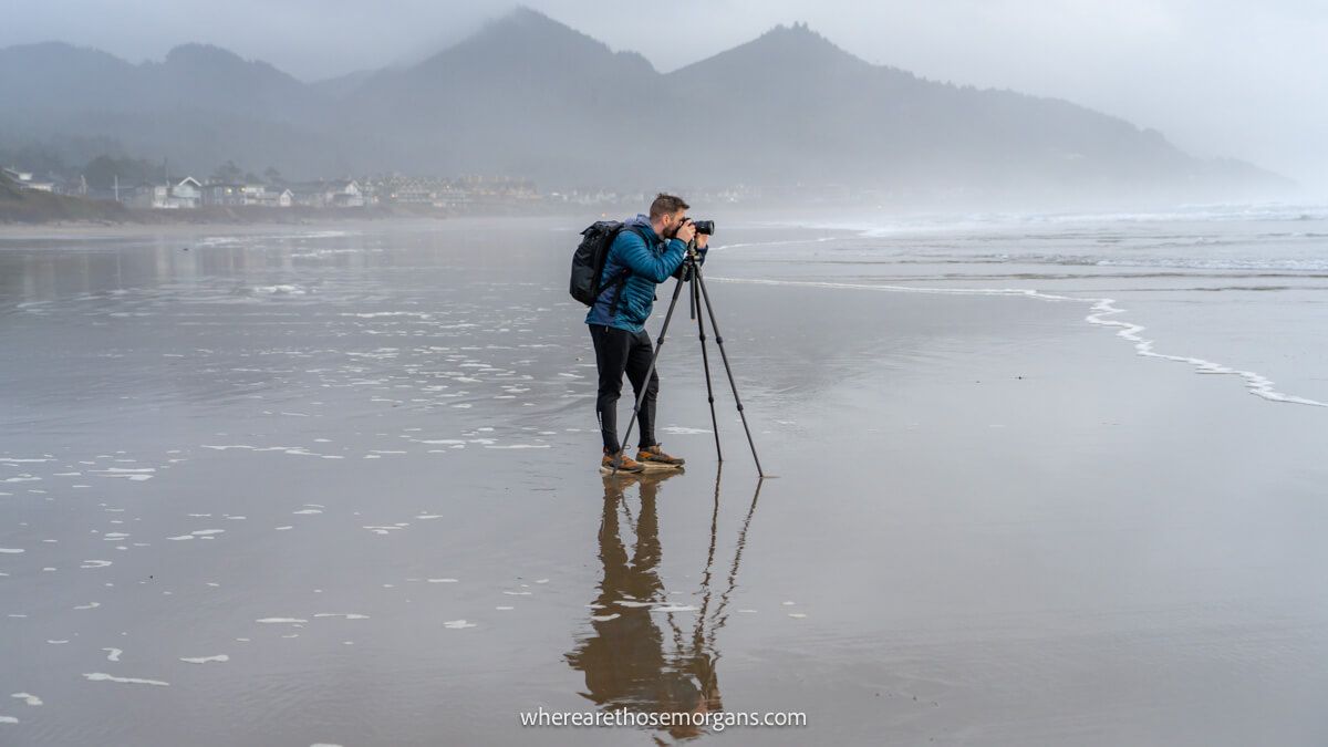Photographer with camera and tripod on a sandy beach covered in water on a foggy day