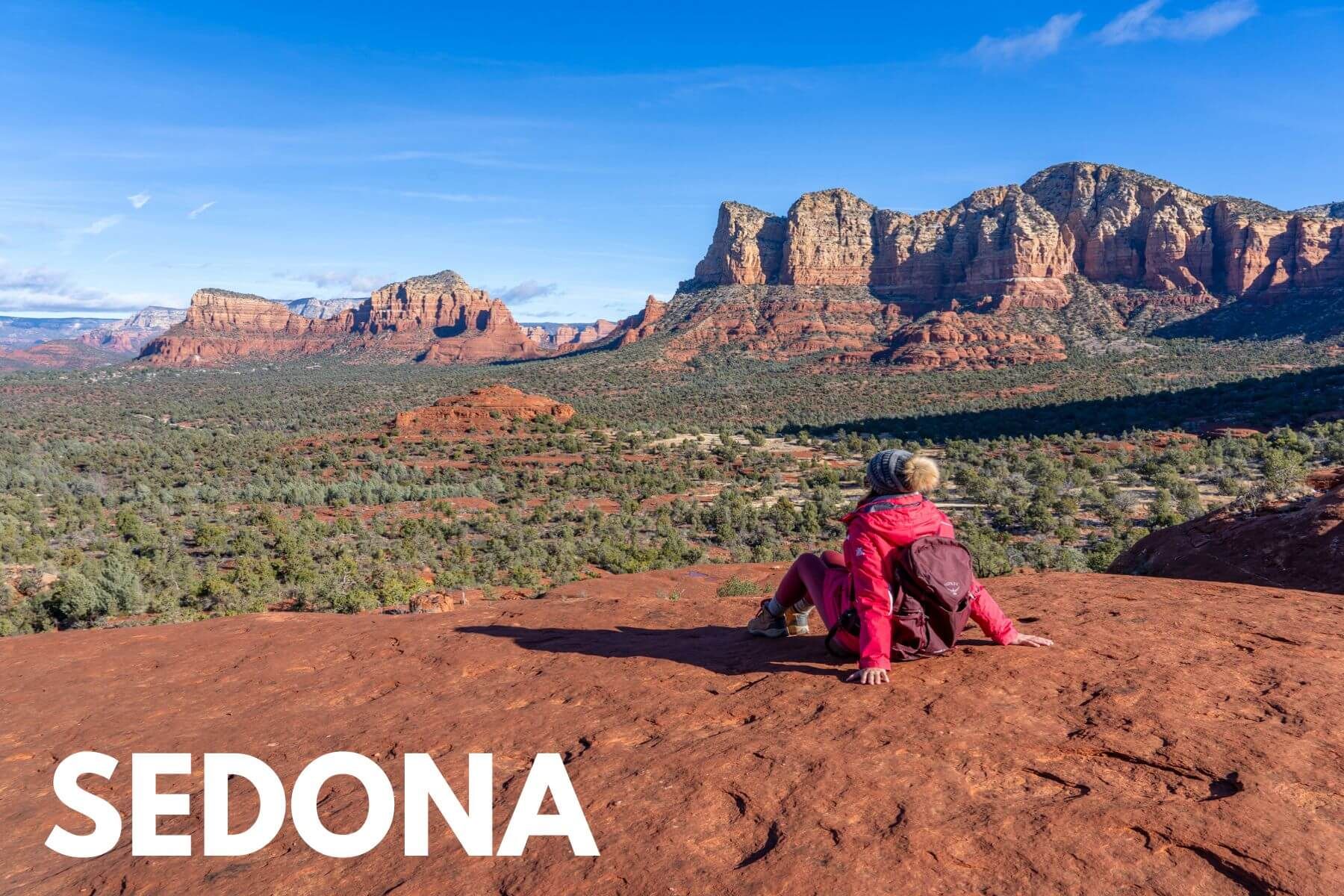 Photo of Kristen Morgan from Where Are Those Morgans sat on red rocks looking out at a wide open view over Sedona AZ valleys and red rock formations under a clear blue sky