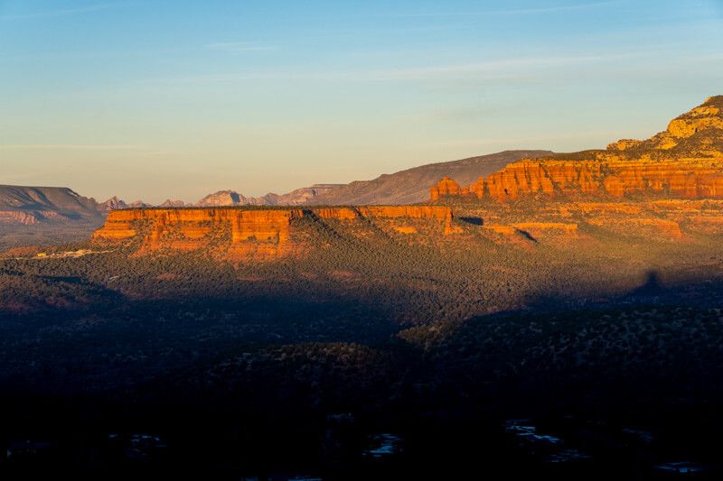 Photo of a sunrise in Sedona with red rocks glowing above deep shadows in a valley