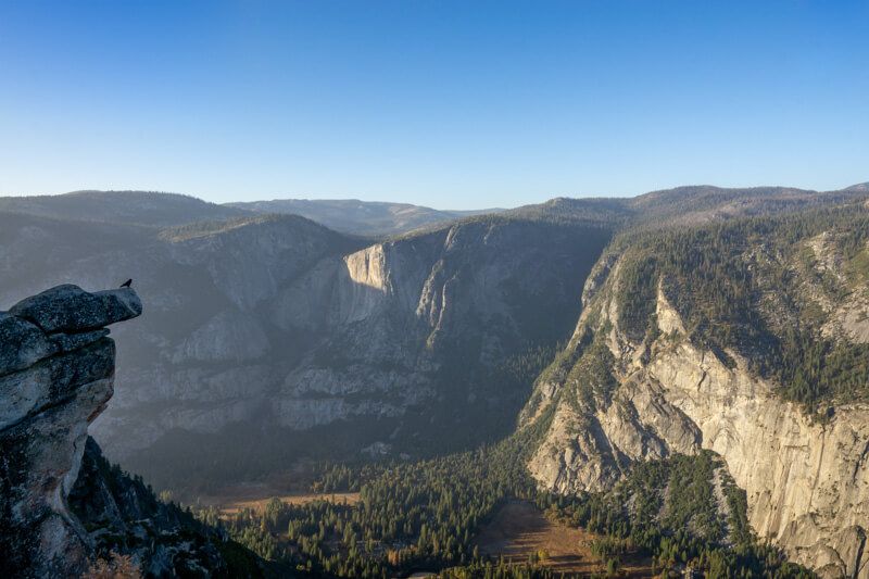 Photo of a deep canyon covered in shadow with distant towering cliffs in sunlight