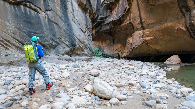Photo of a hiker on a rocky beach in waterproof pants and shoes inside a narrow river slot canyon in Zion