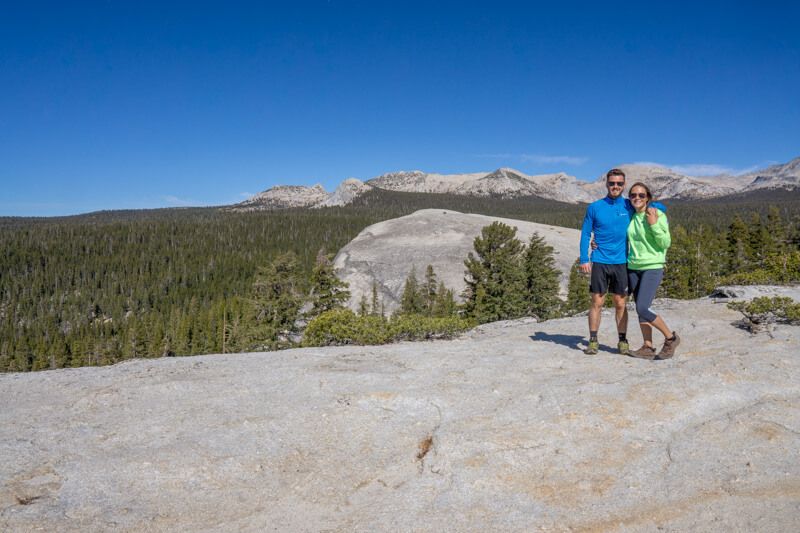 Photo of Mark and Kristen Morgan standing together on a granite rocky surface with wide open views over trees and granite formations in Yosemite