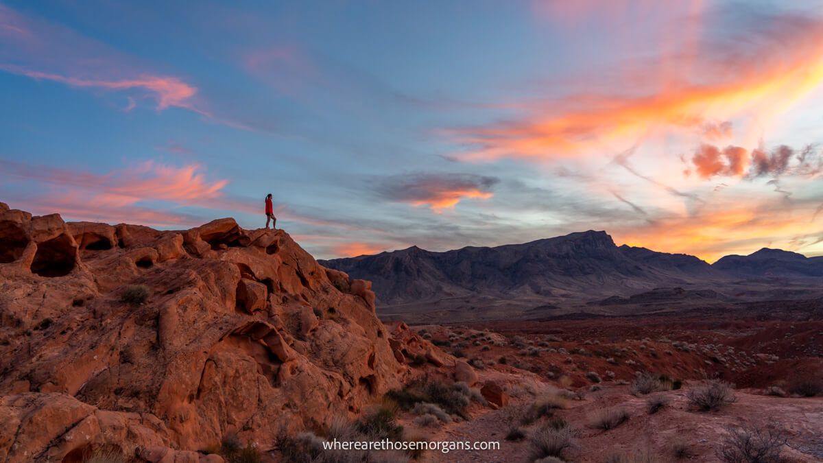 Photo of a hiker in the distance stood on a rocky ledge in a red rock landscape at sunset in Valley of Fire State Park, Nevada