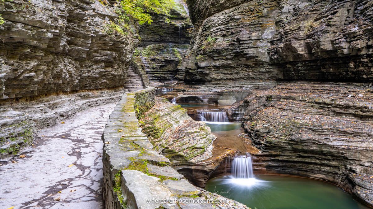 Photo of a series of small waterfalls plunging through a narrow gorge next to a stone walkway
