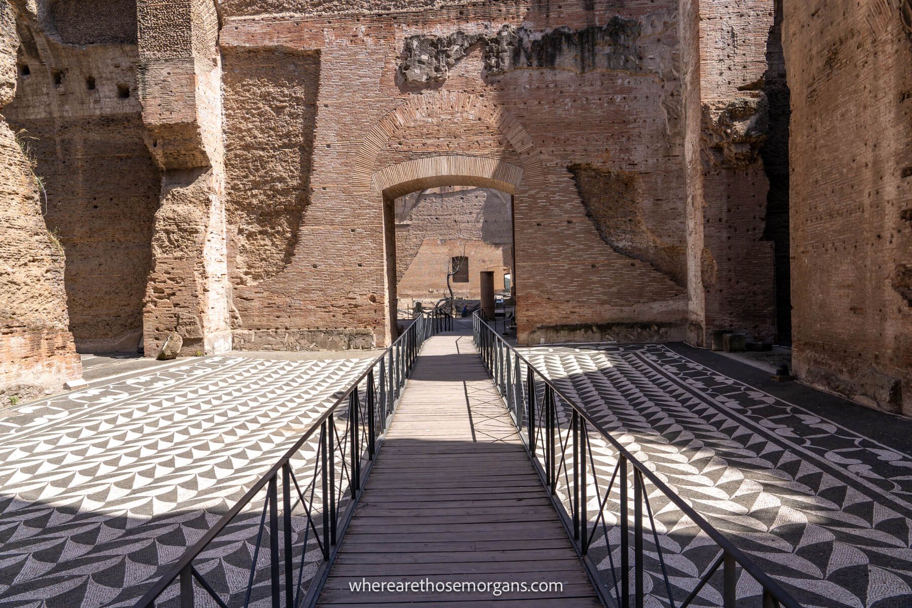 Photo of a pedestrian walkway with black metal fences going through an old brick ruin with mosaic floors in the Caracalla Baths in Rome