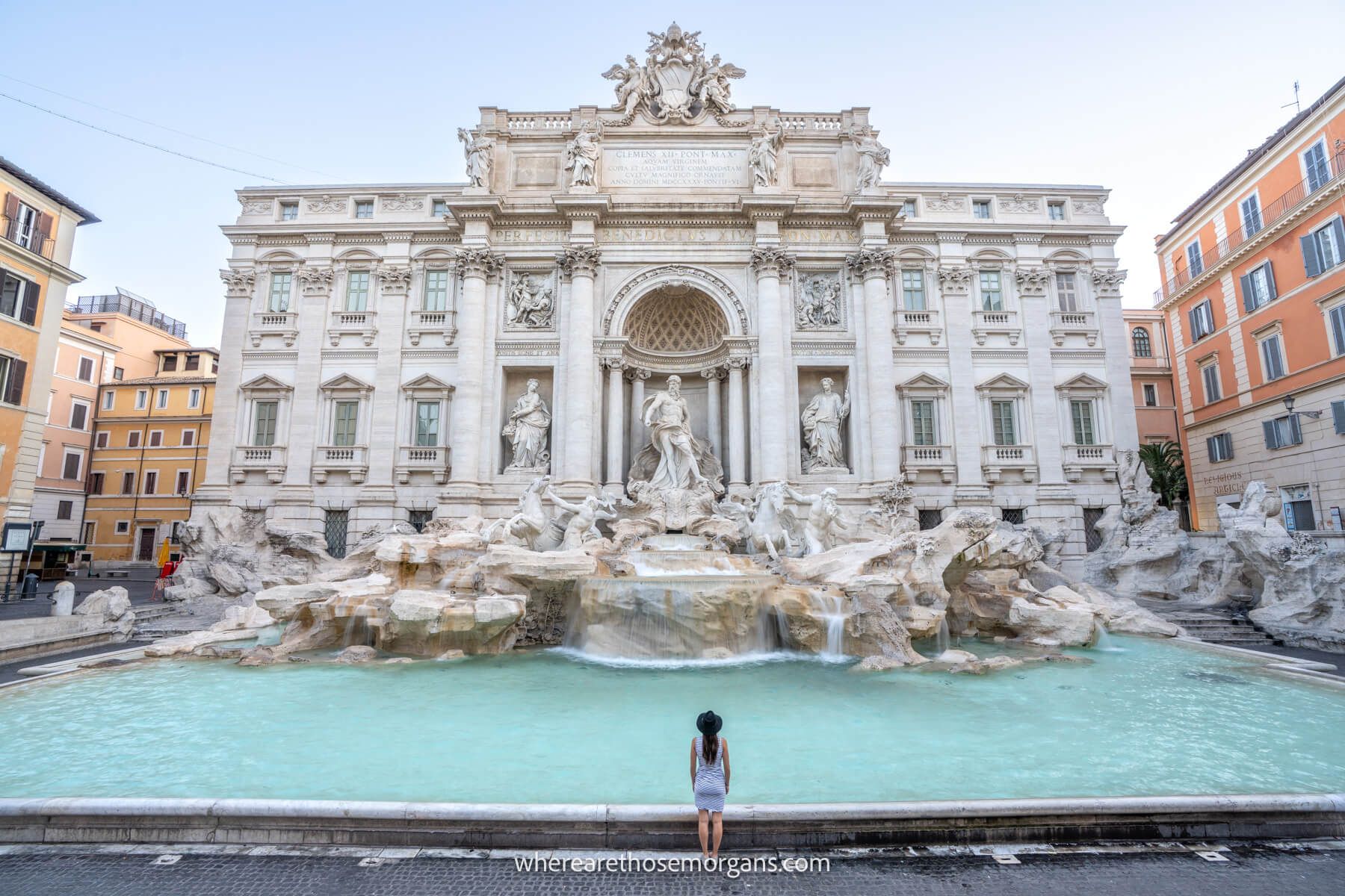 Photo of a tourist standing alone in front of the Trevi Fountain in Rome's Centro Storico at dawn