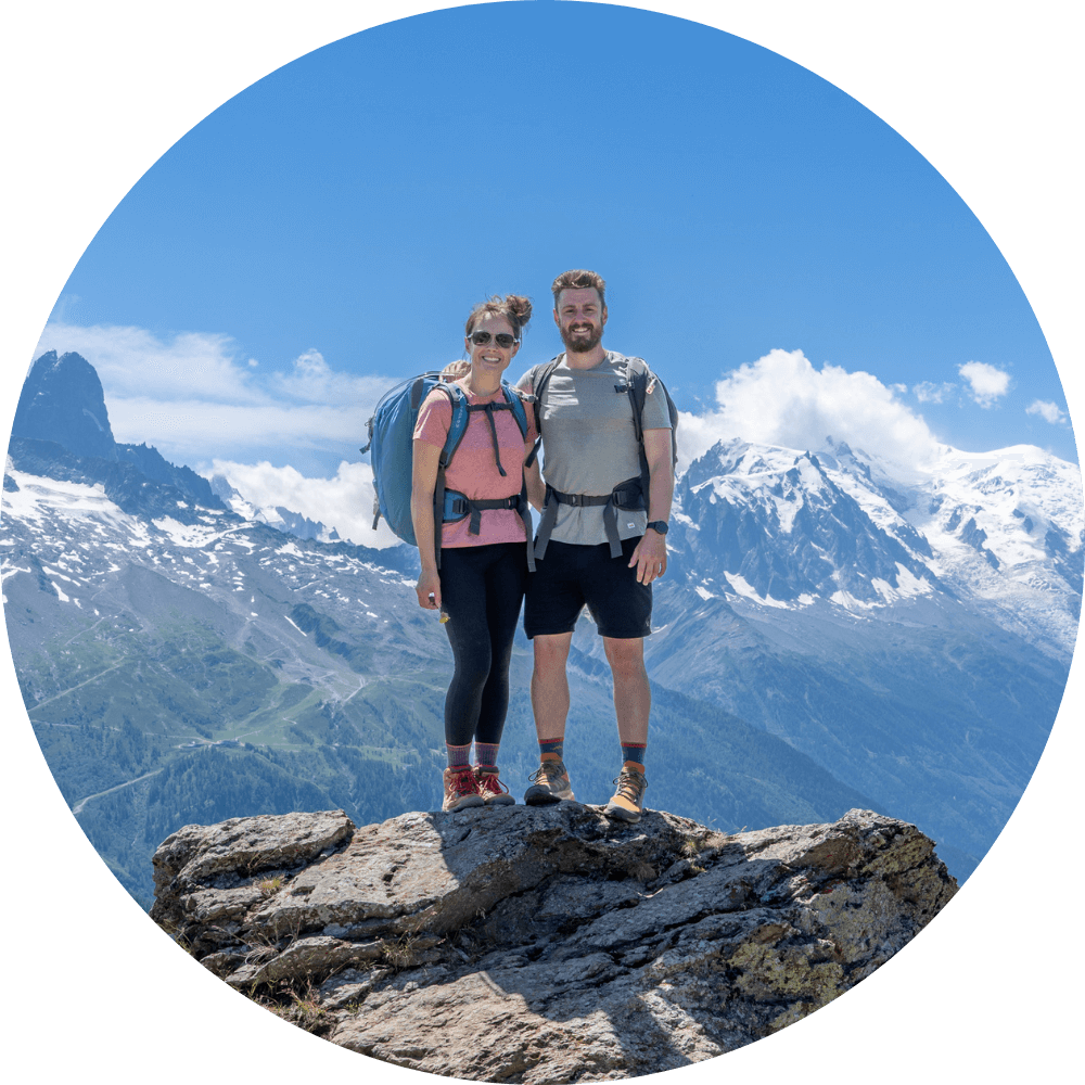 Photo of Mark and Kristen Morgan from Where Are Those Morgans travel blog standing on a boulder in hiking gear with mountains in the background on a sunny day with blue sky