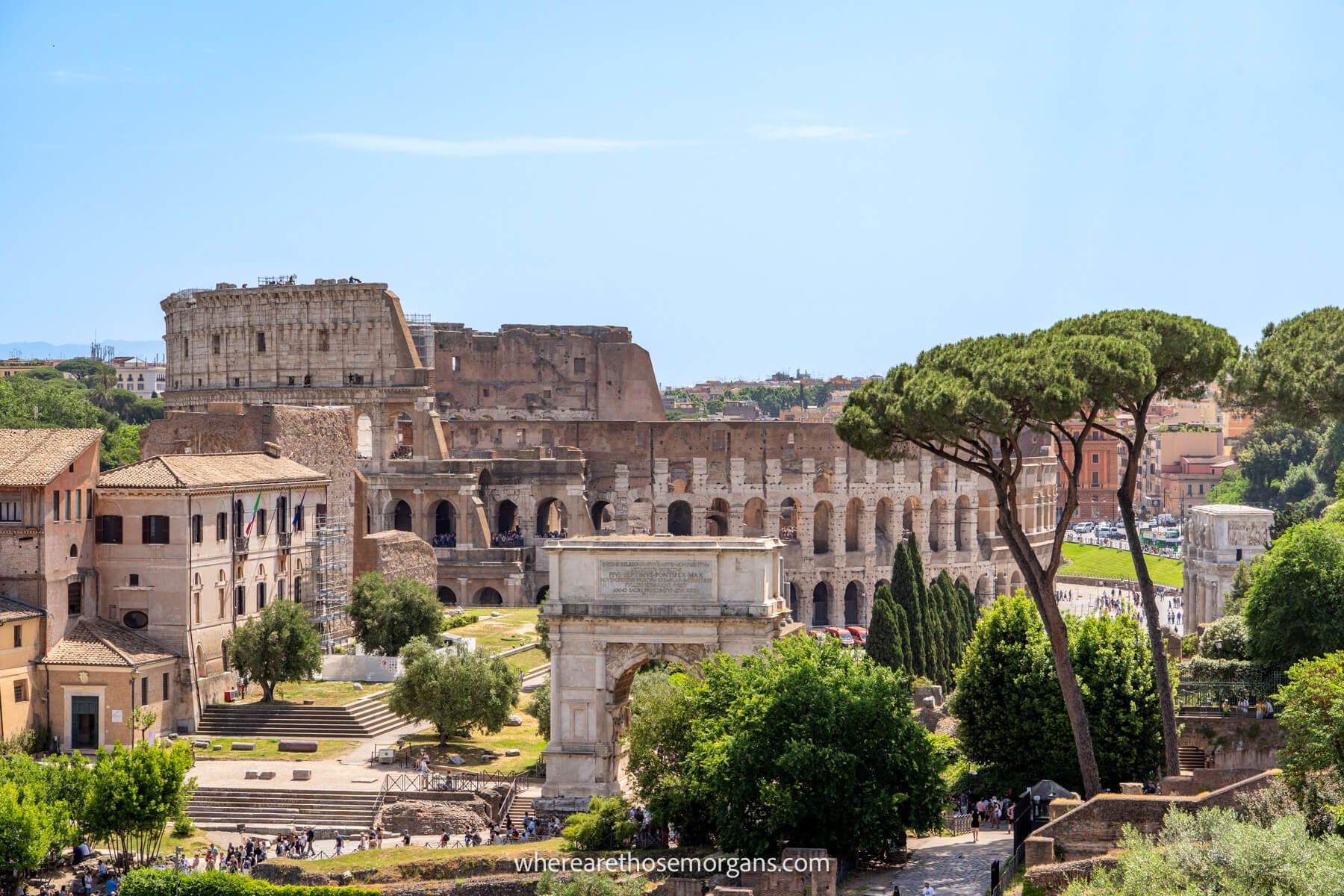 Photo of ruins, arches, trees and the Flavian amphitheater from a viewpoint in Rome under a clear blue sky