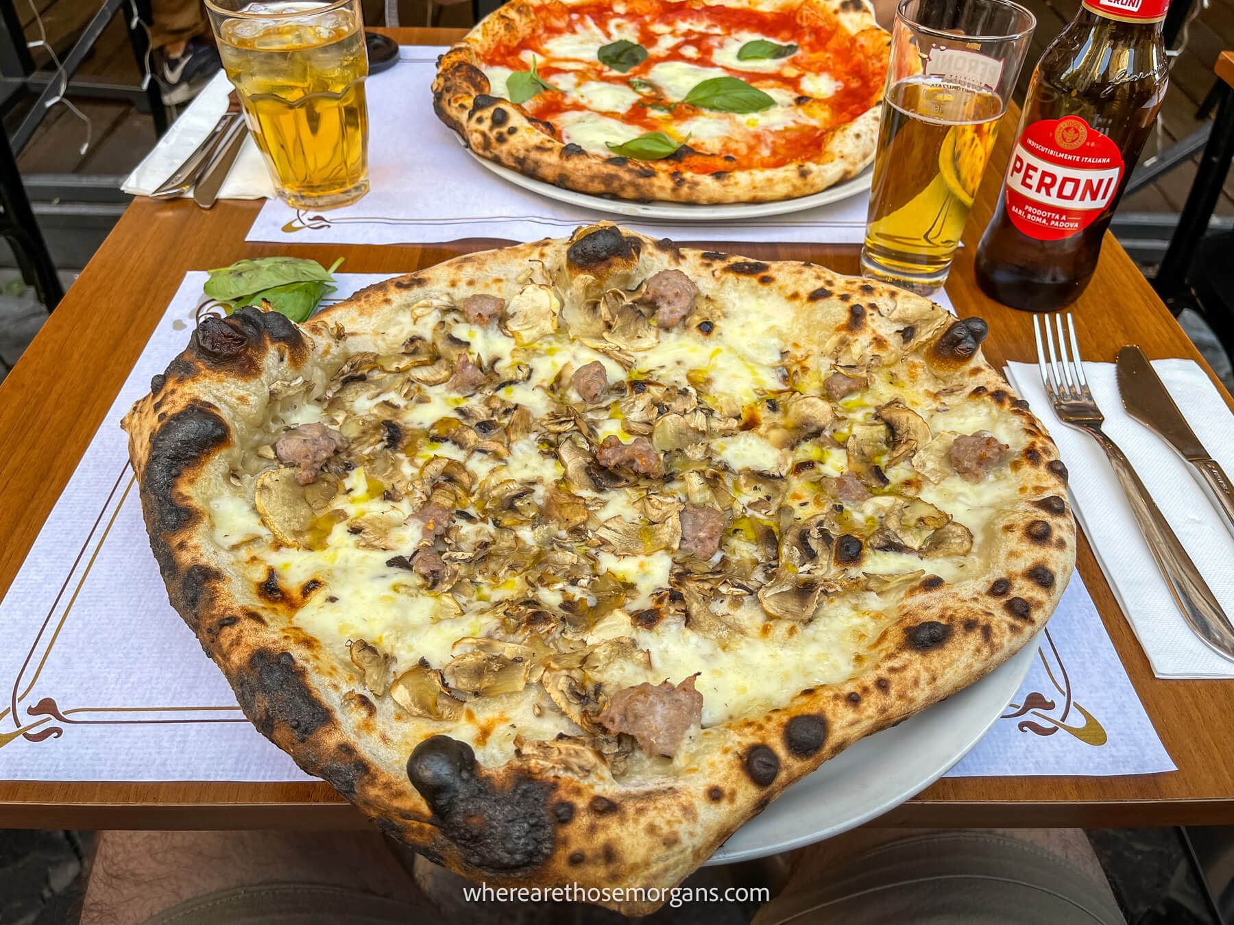 Photo of two pizzas on a table with a beer and cocktail