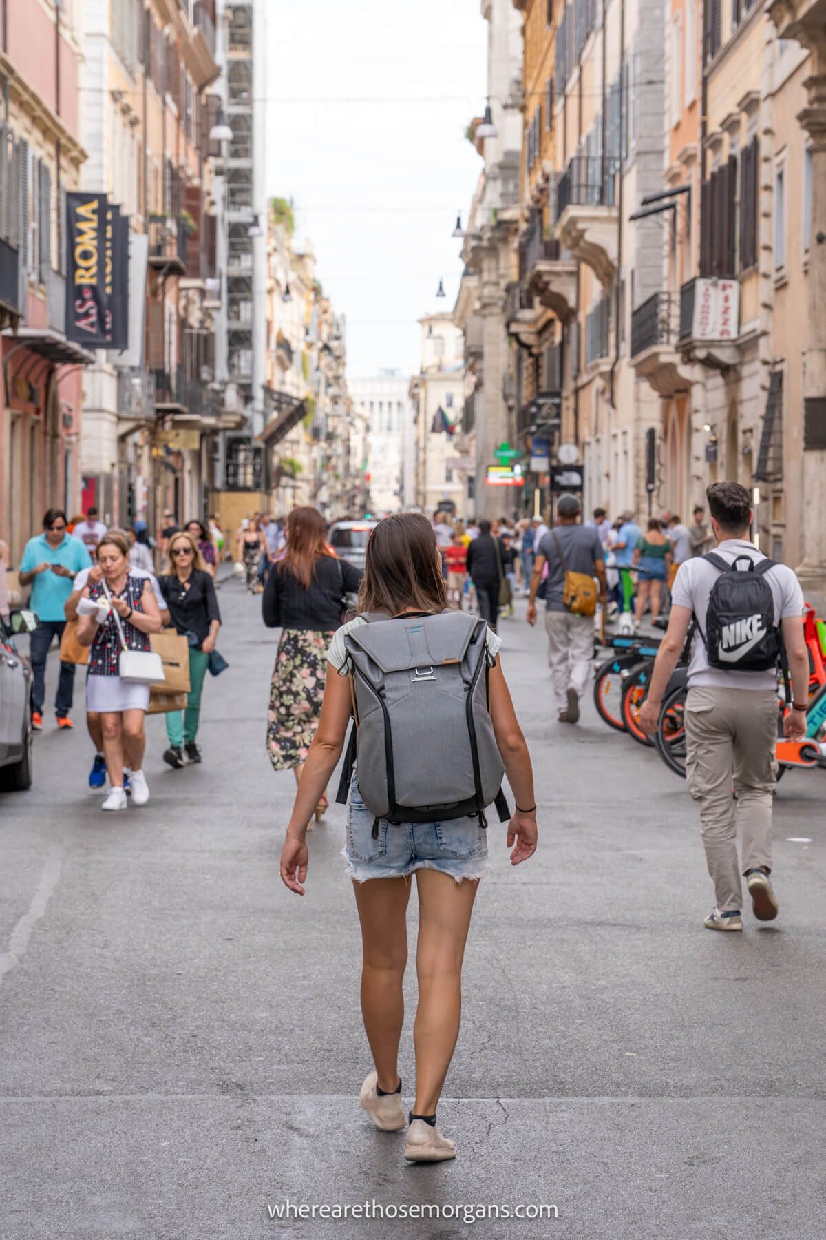 Photo of a tourist walking up a narrow shopping street in Rome among lots of locals and tourists