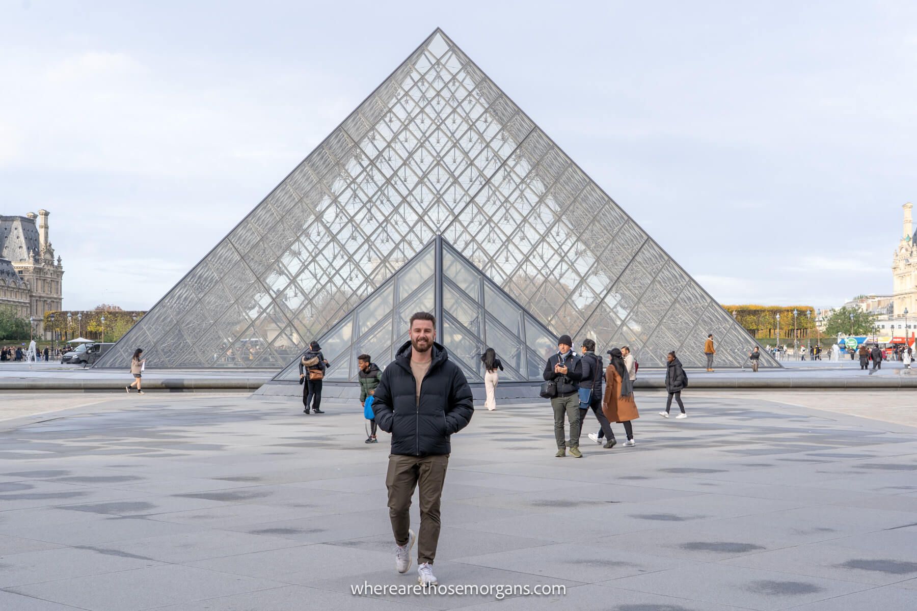 Photo of Mark Morgan walking in front of the glass pyramid at the Louvre