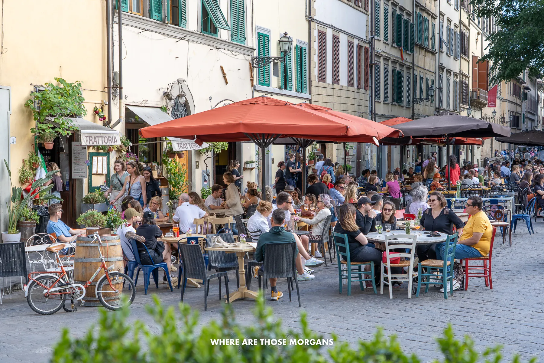 Crowds of people sat on outdoor tables under umbrellas in a Florentine neighborhood