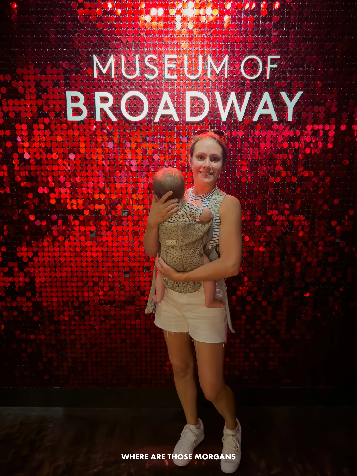 Photo of a tourist standing underneath the Museum of Broadway sign with a baby
