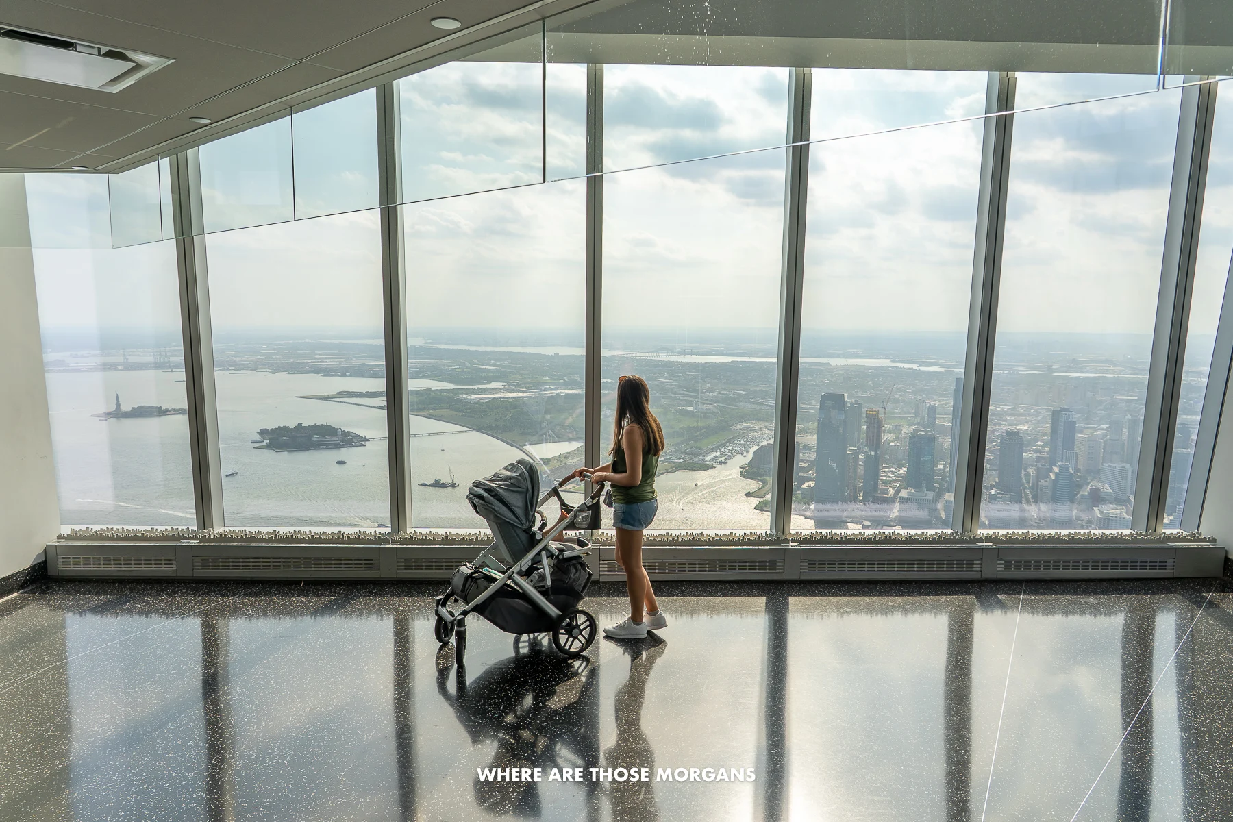 Photo of a tourist walking with a stroller in front of tall windows at the top of One World Observatory