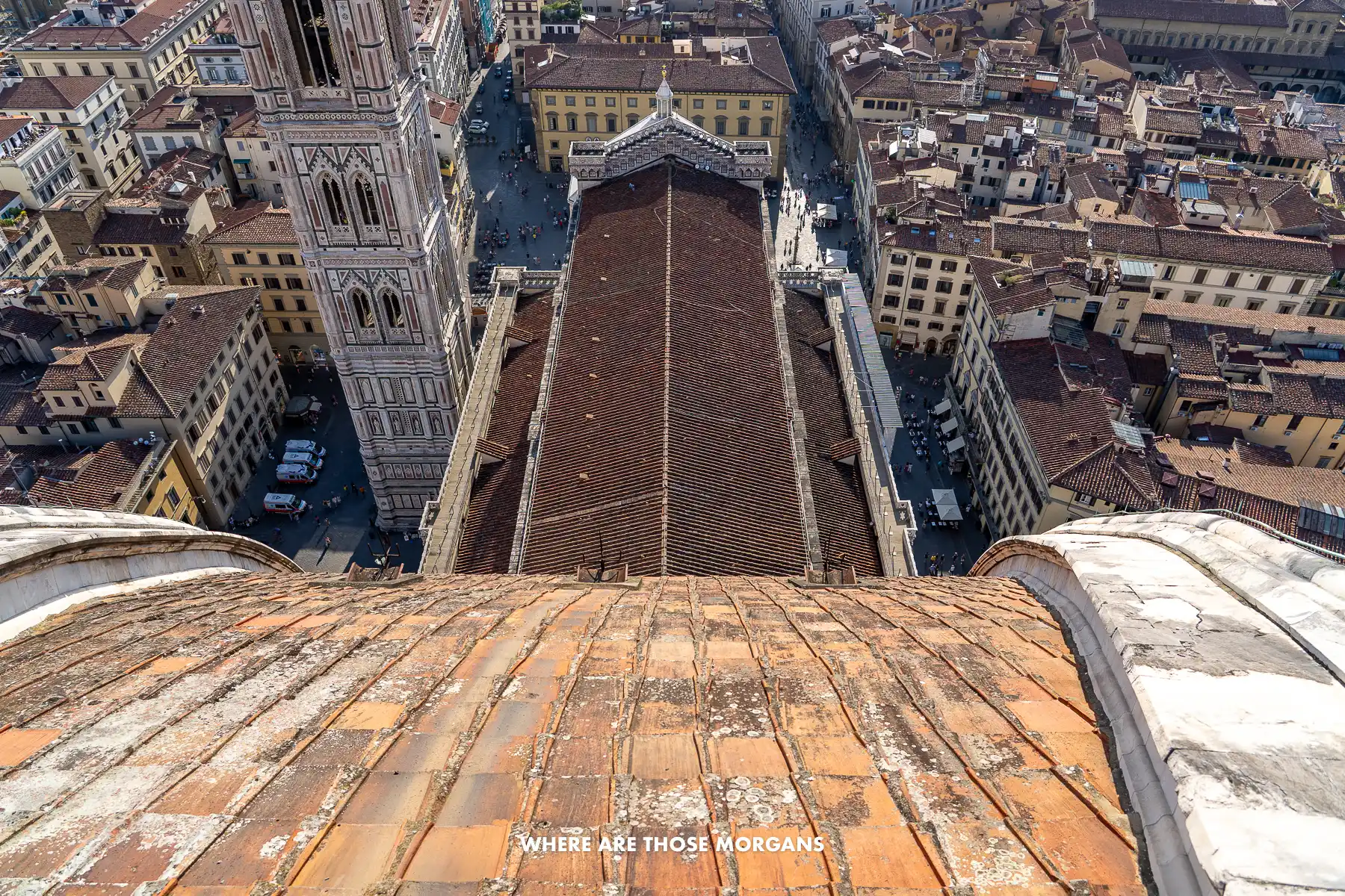 Photo looking down on a sloping cathedral tiled roof from high up overlooking a city in Tuscany