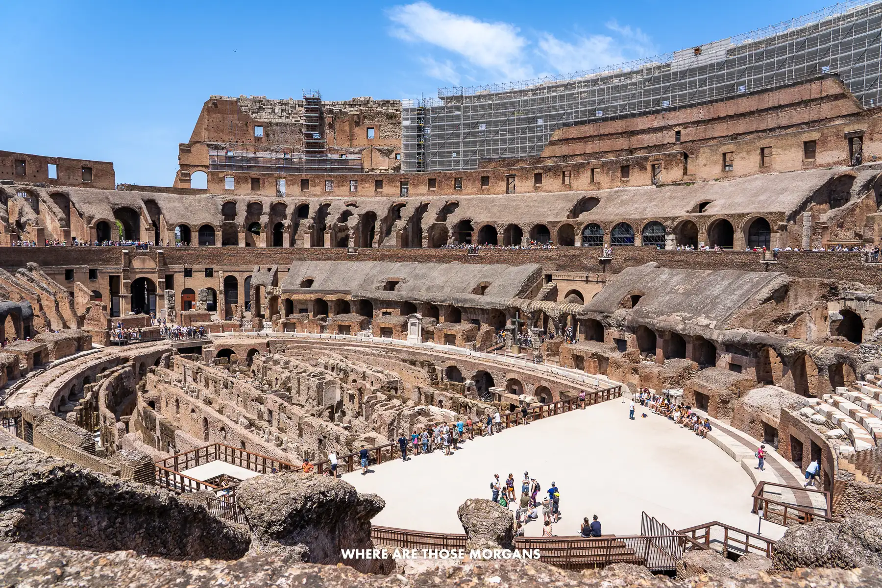 Photo of the inside of Rome's Colosseum with tourists on the Arena floor and walking around the upper levels on a clear and sunny day