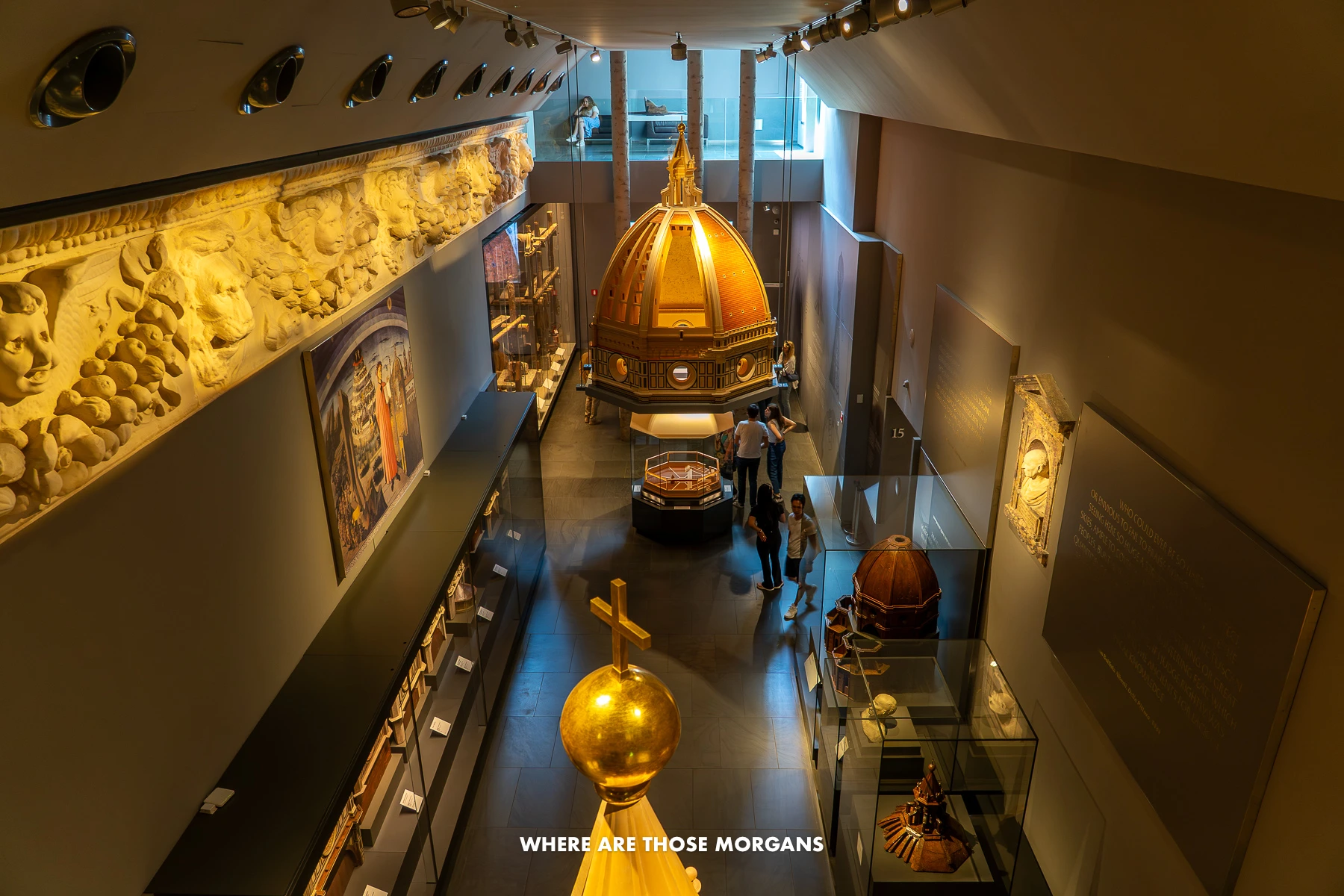 Photo of the inside of Opera del Duomo Museum in Florence with tourists looking at original art works in a dark room with dim yellow lighting