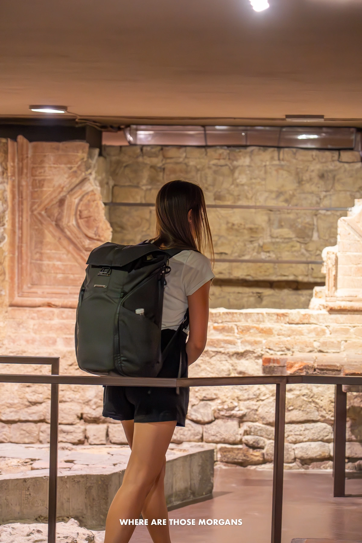 Photo of a tourist walking through Santa Reparata Crypt underneath a church in Italy with lights on a low ceiling lighting up tombs and ruins