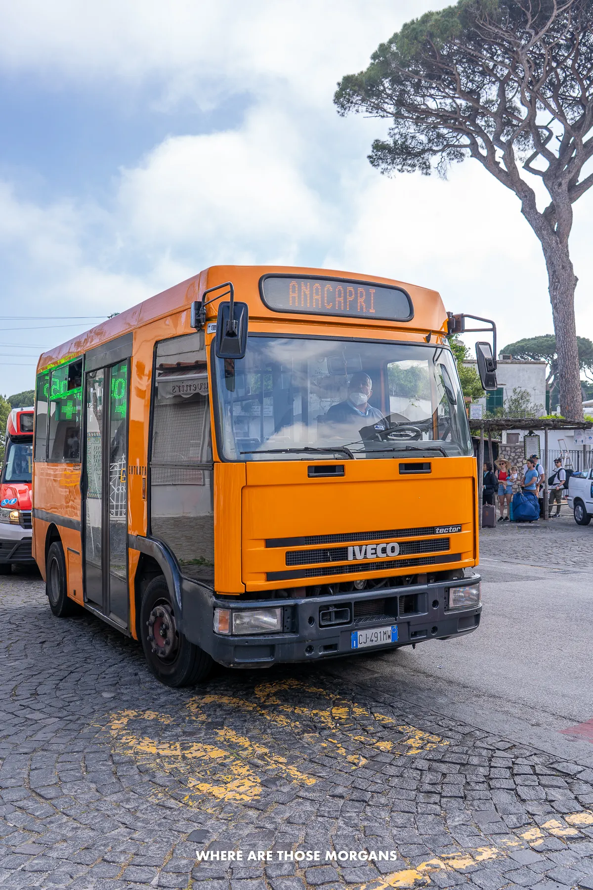 Photo of a small orange bus at a bus stop in Italy