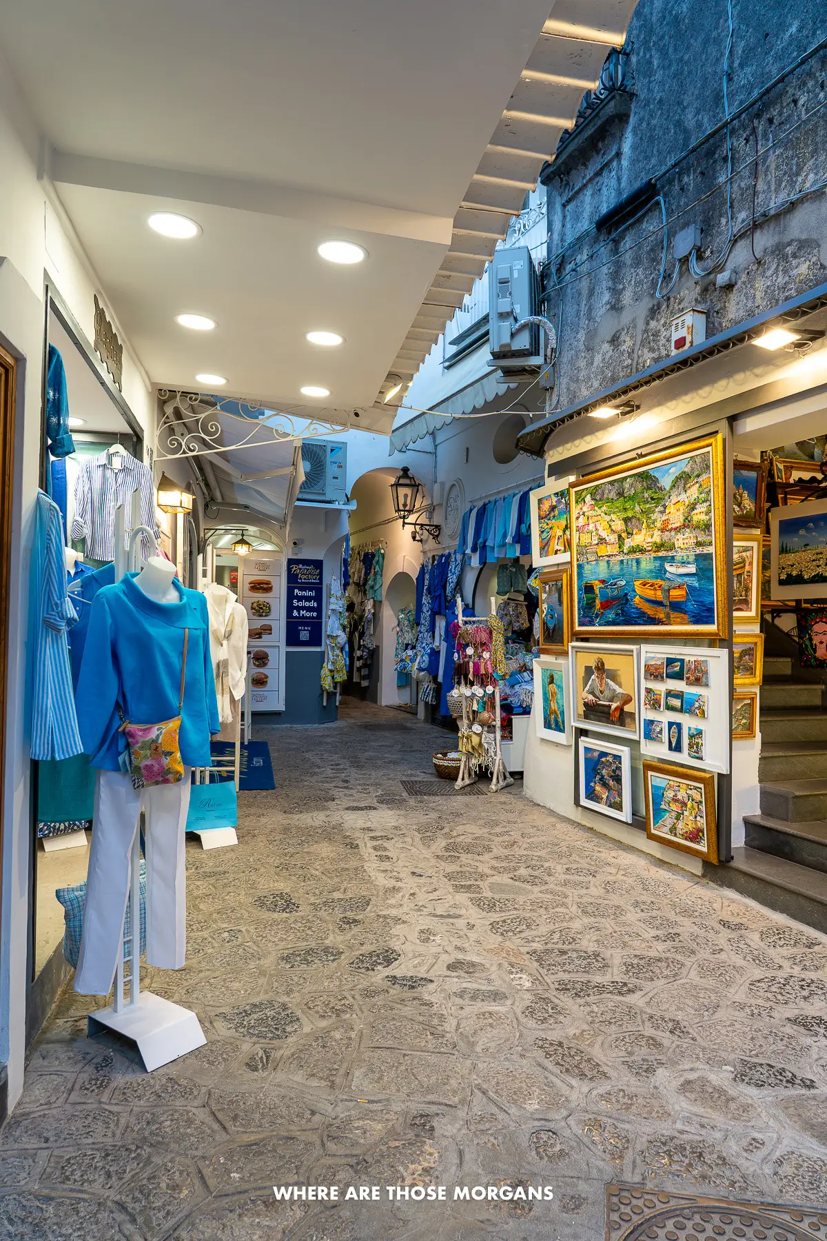 Photo of a narrow cobbled shopping street with paintings and photos in Positano