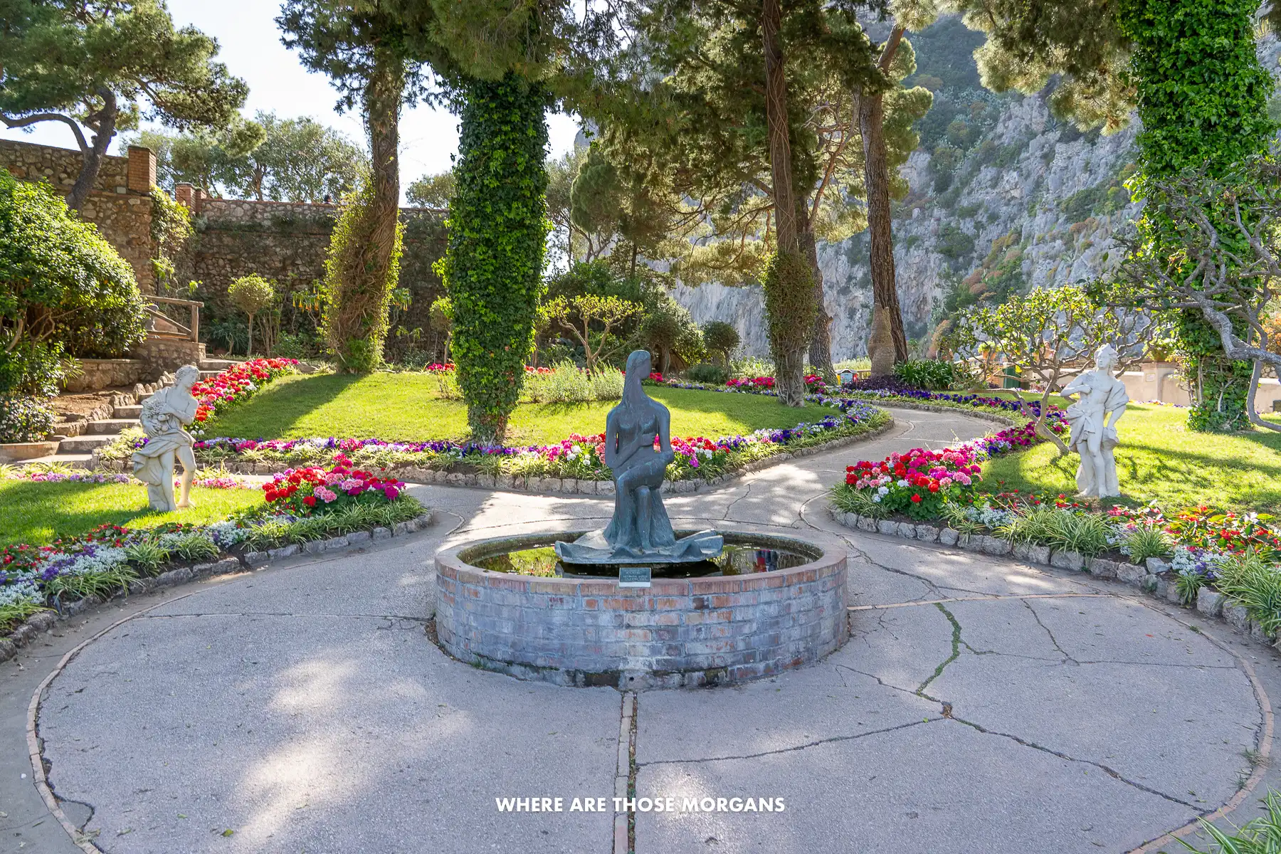 Photo of a small statue in a garden with colorful flowers and trees
