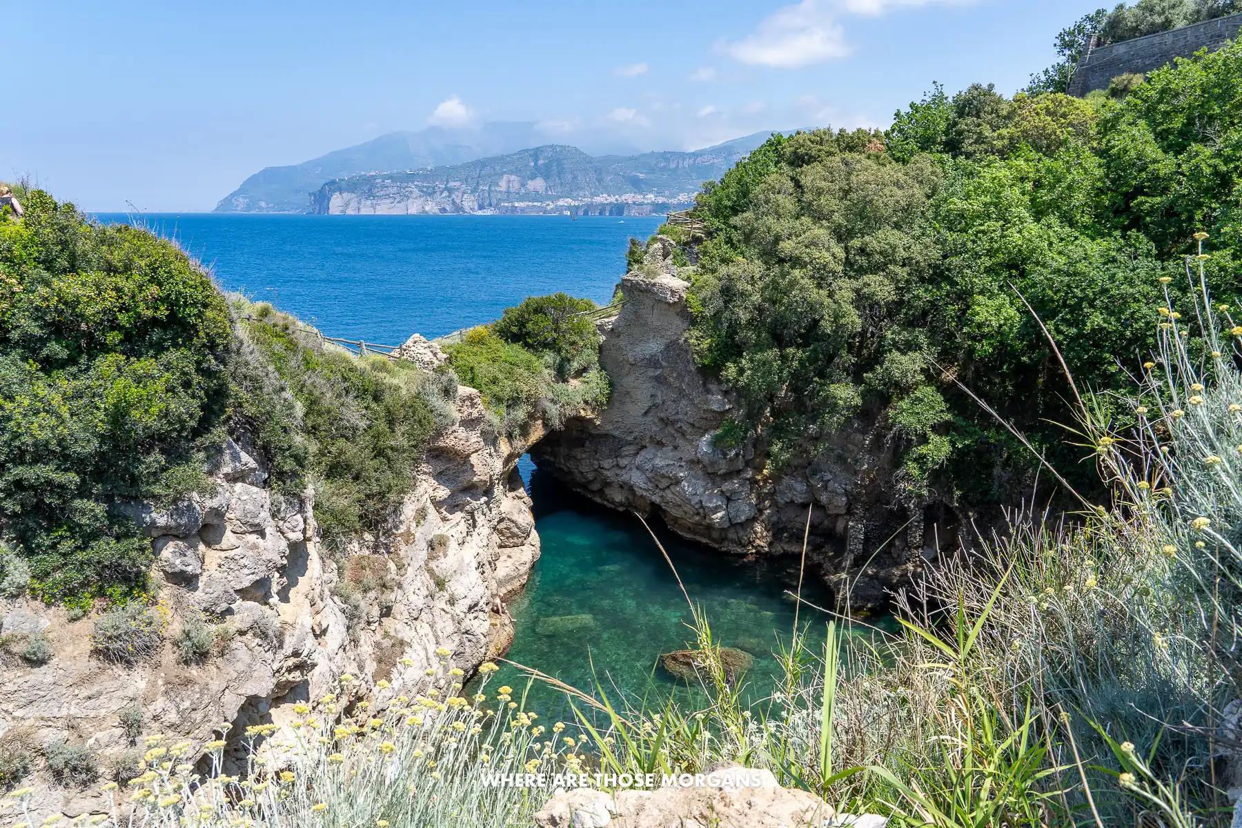 Photo of a cove with clear water and a small arch leading back out to sea from a headland in Italy