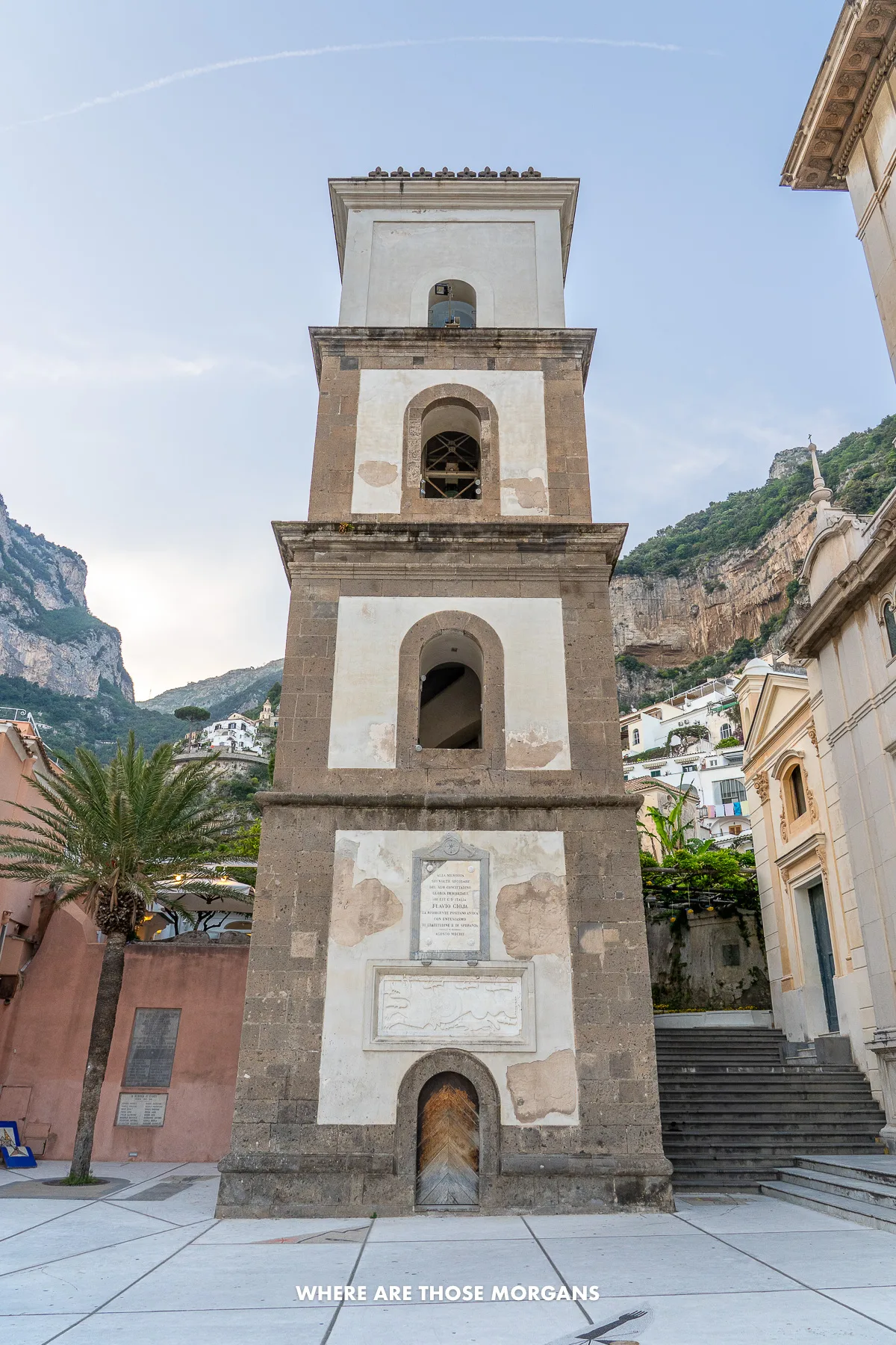 Photo of a tall cuboid-shaped bell tower in a small piazza in Italy