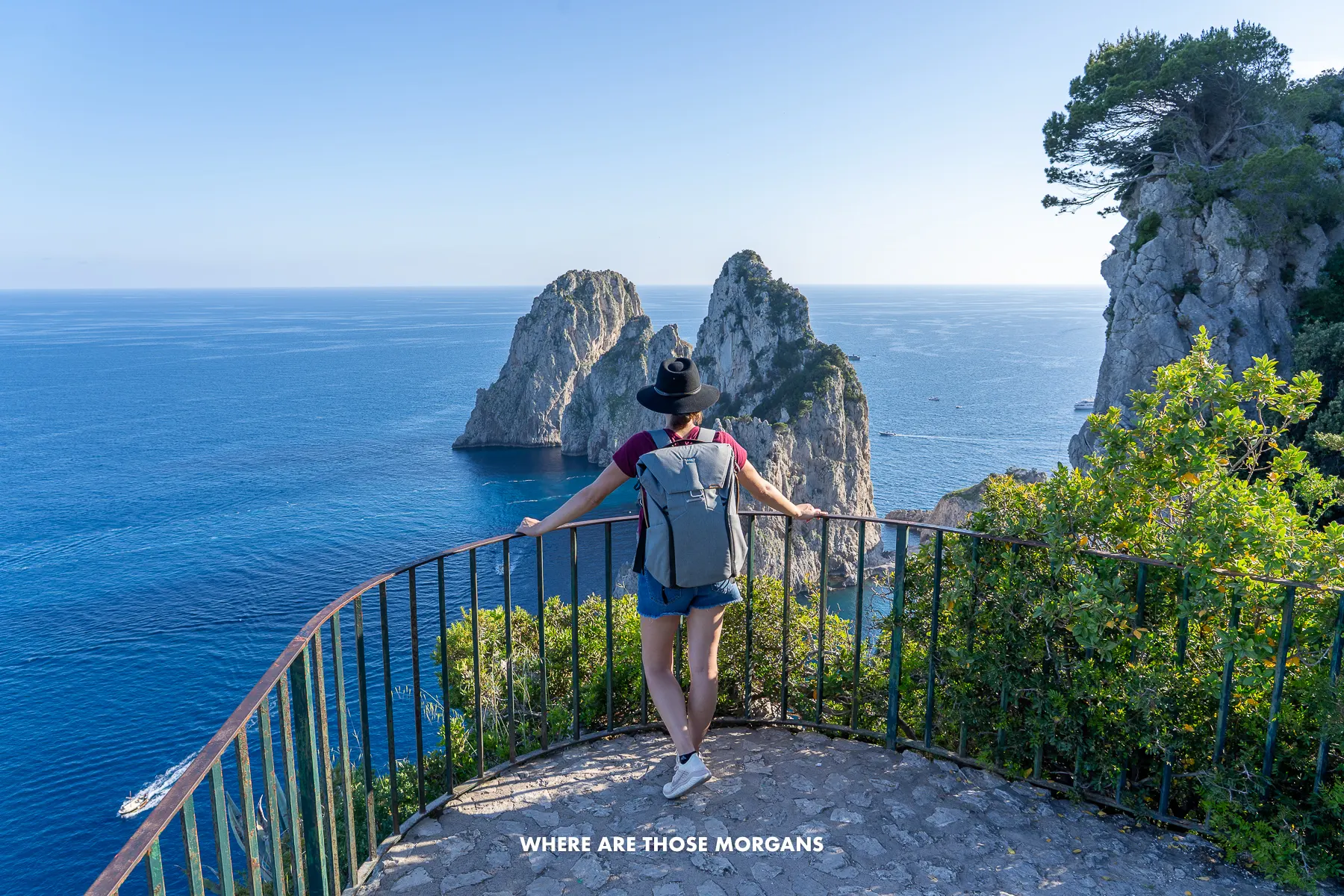 Photo of Kristen Morgan from Where Are Those Morgans standing against a black metal fence looking out at the sea and sea stacks in Capri Italy