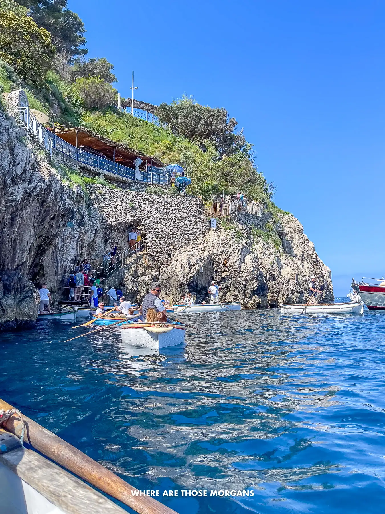 Photo of a line of boats on a cliffside in the sea waiting to go inside a cave