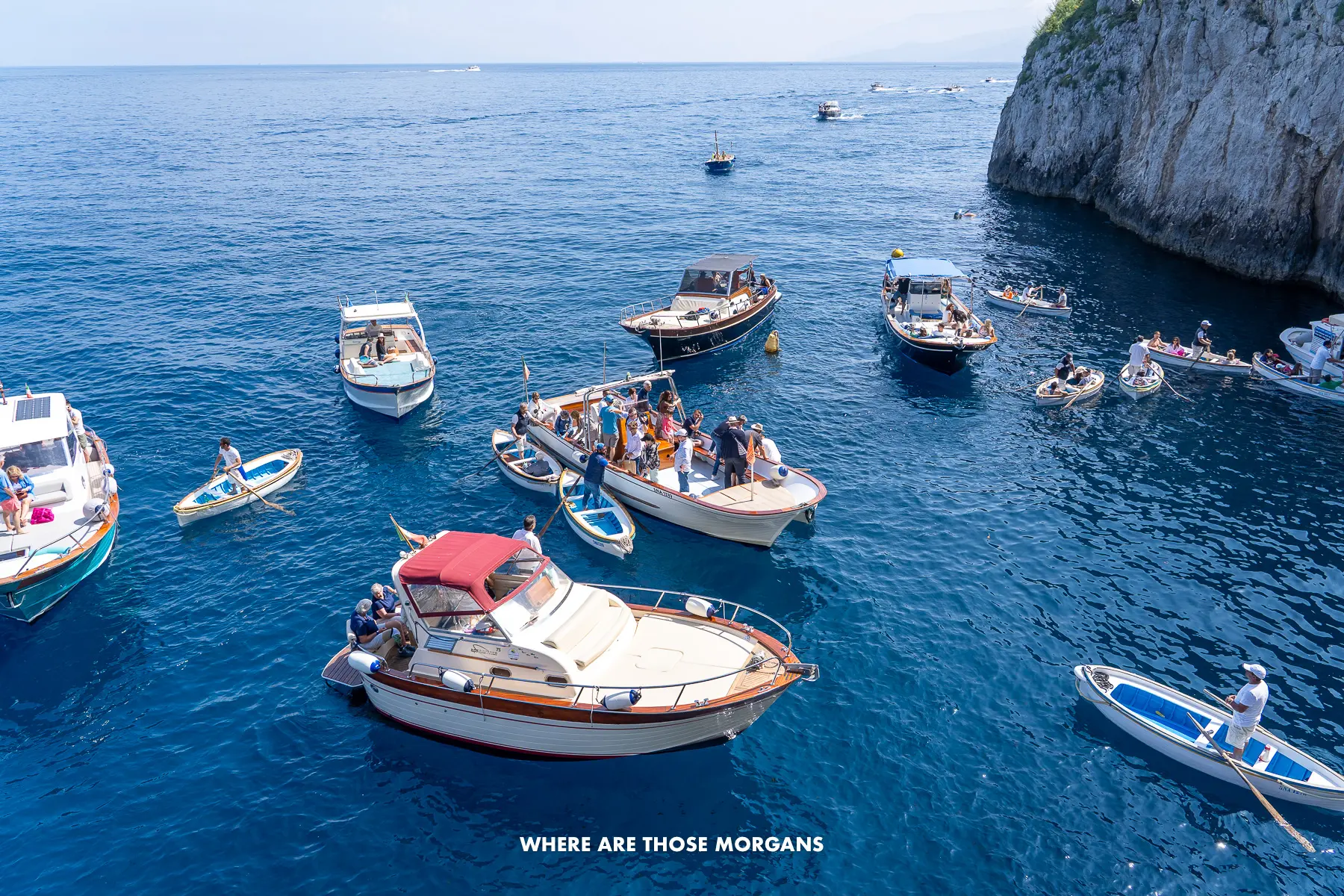 Photo of several small boats anchored at sea outside a sea cave in Capri Italy