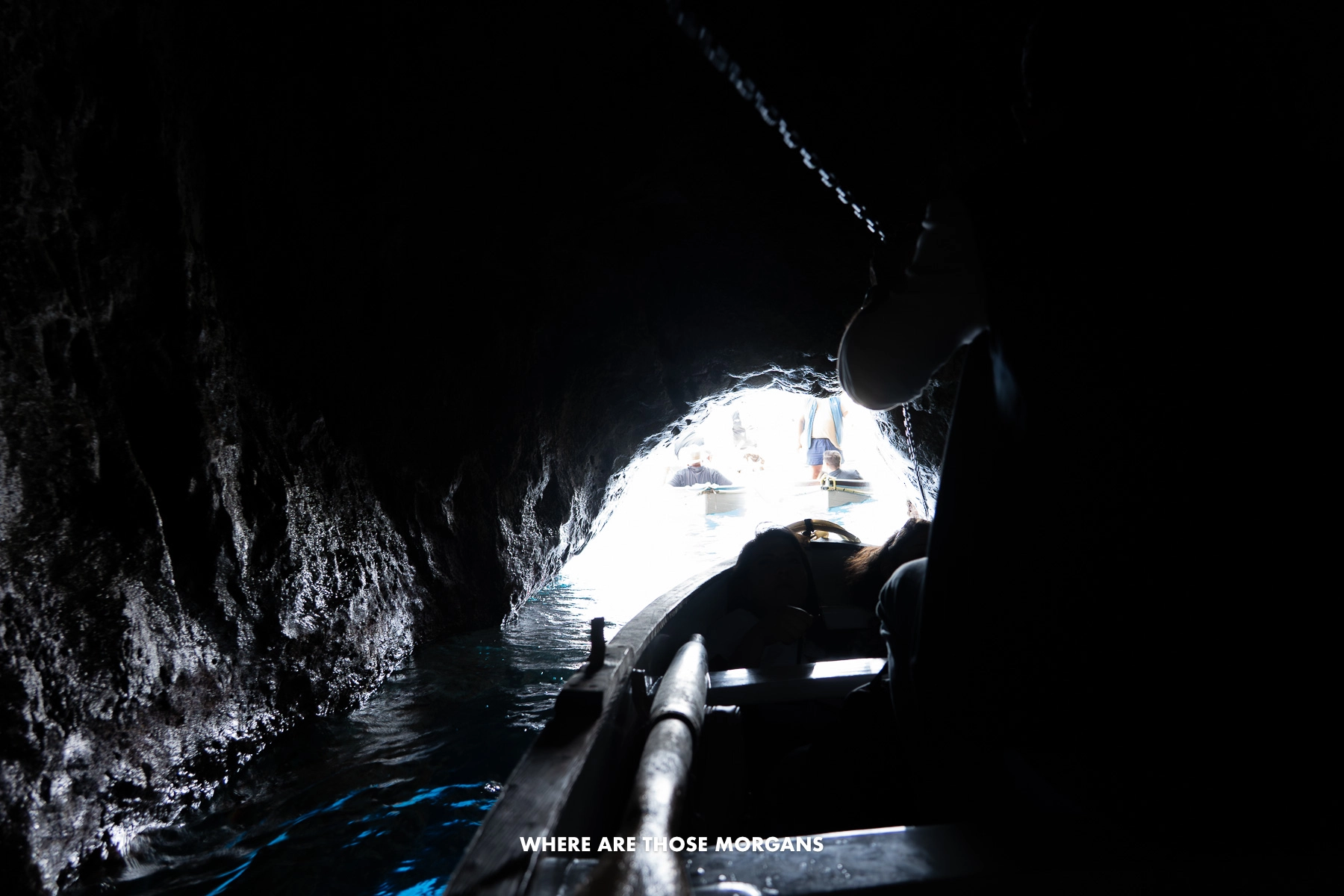 Photo of a small rowing boat exiting a sea cave in the darkness towards the bright tunnel-like outside world