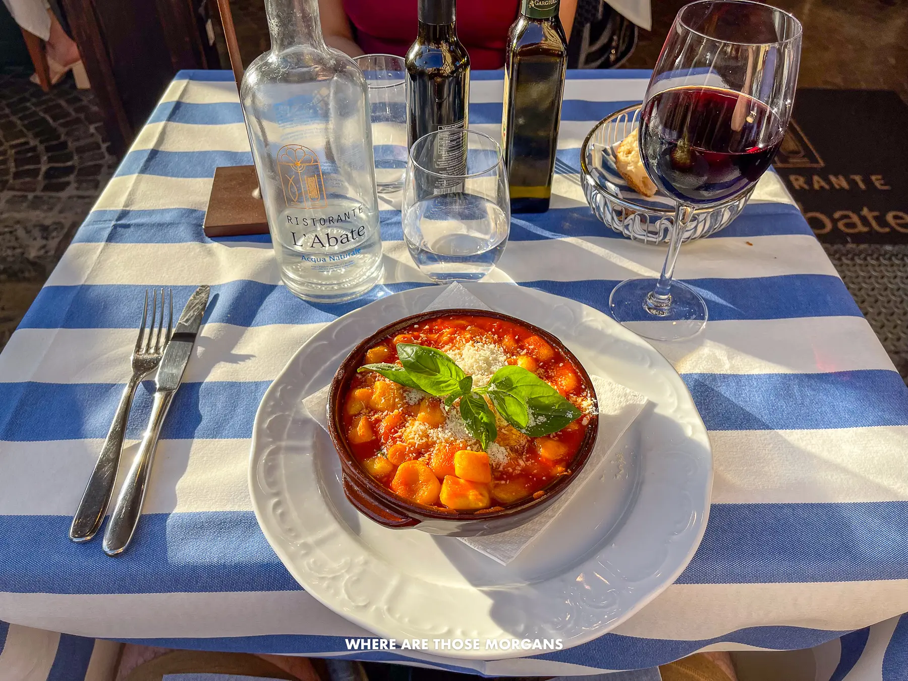 Photo of gnocchi alla sorrentina on a table with wine and a blue and white striped table cloth