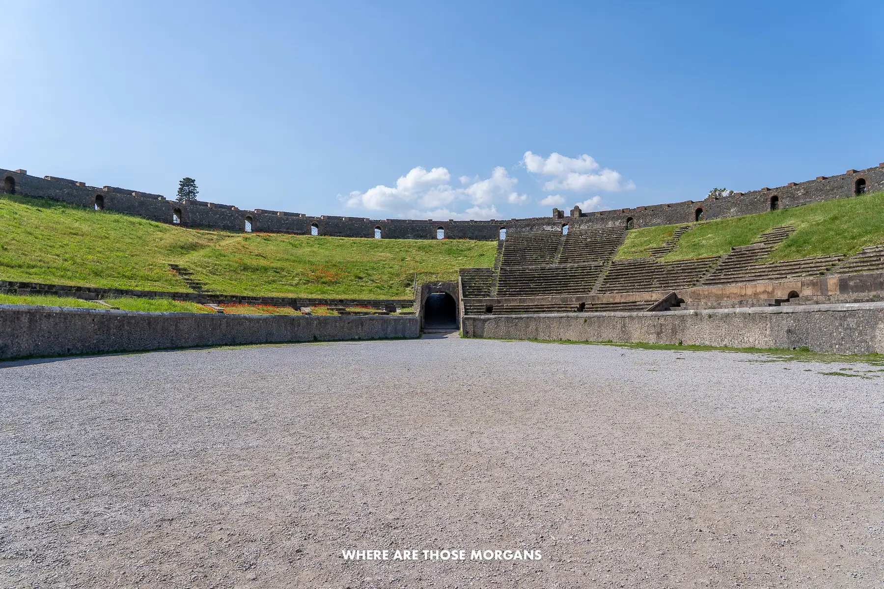 Photo taken inside an ancient amphitheater in Italy with gravel on the ground and grass growing in the stands