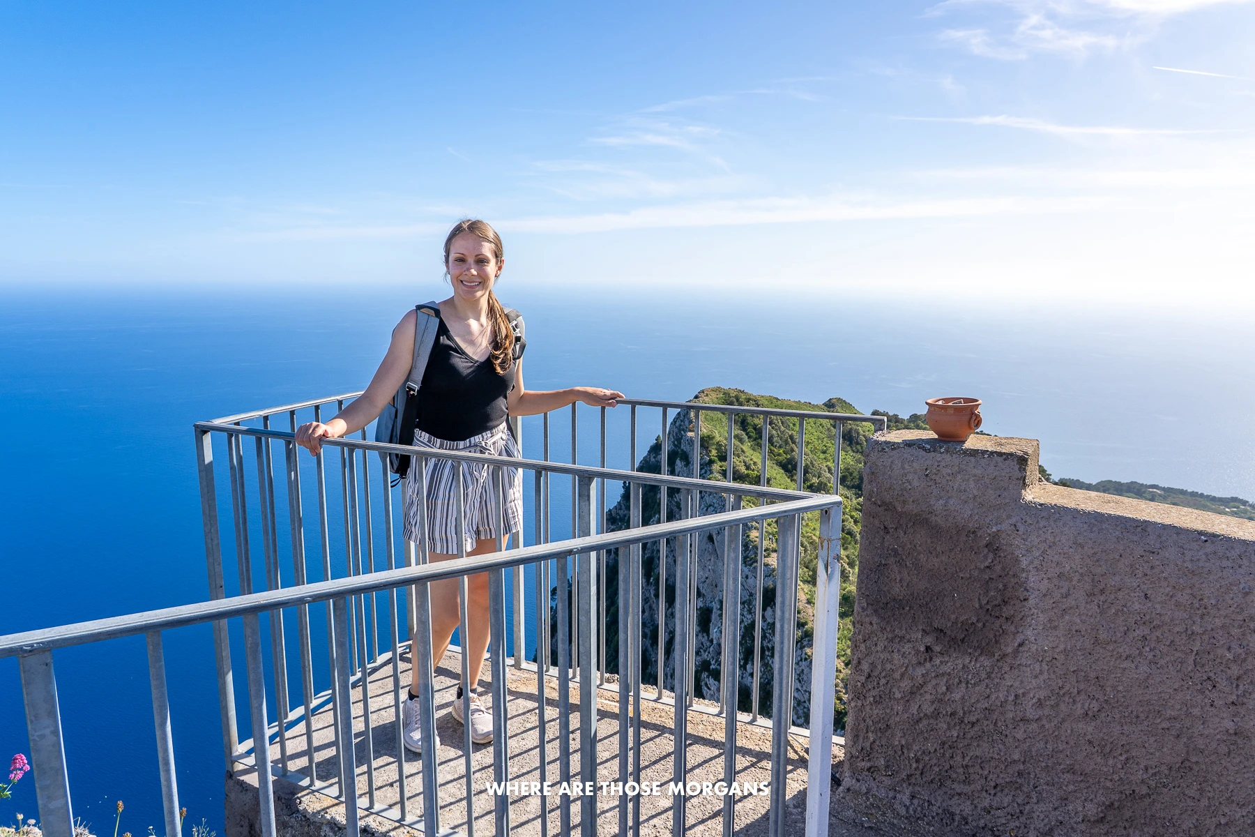 Photo of Kristen from Where Are Those Morgans standing on a small platform with rails for a photo with nothing but sea and sky behind at the summit of Monte Solaro in Capri, Italy