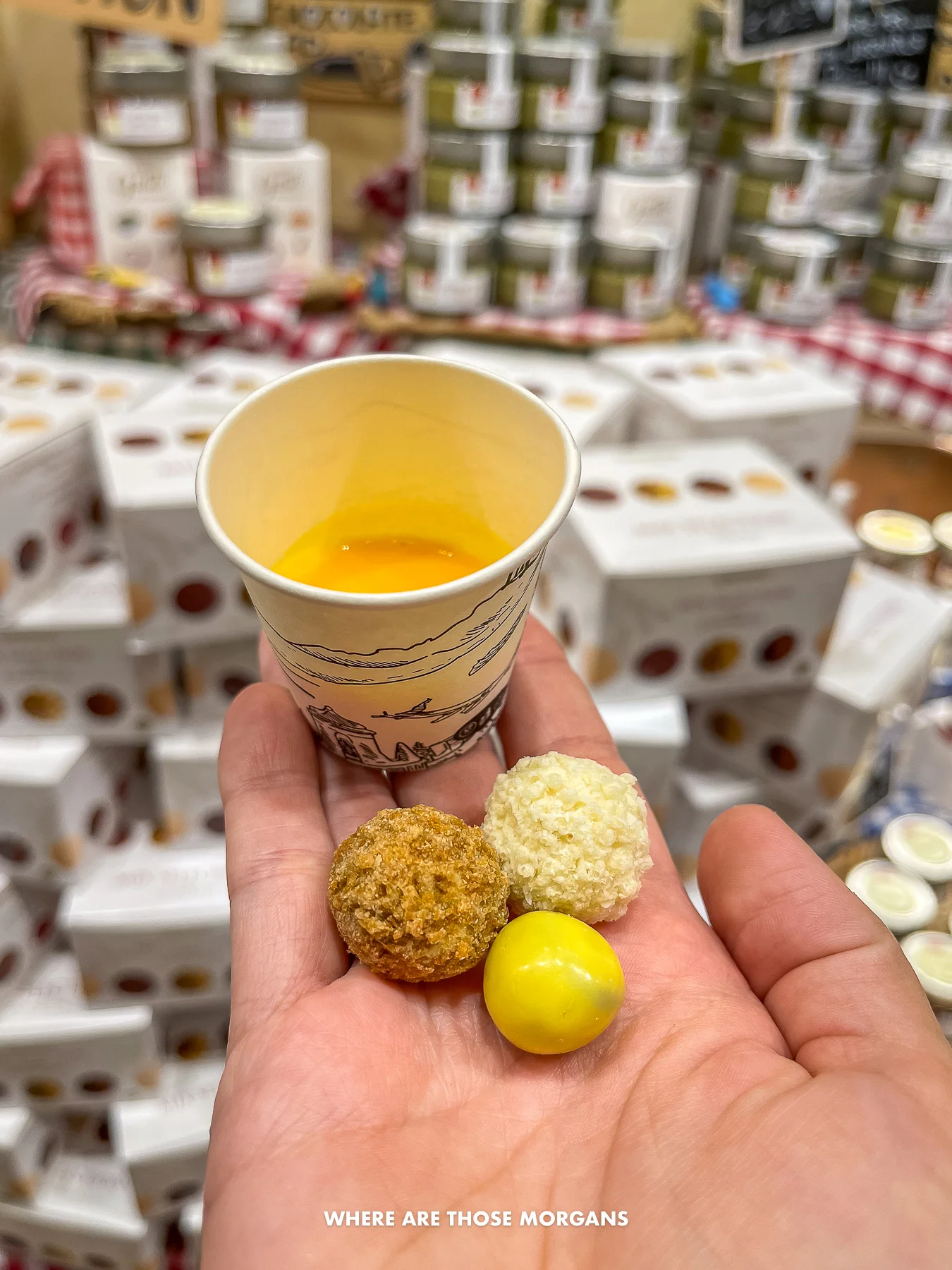 Photo of an outstretched hand holding aa small sample cup filled with limoncello and three types of nut