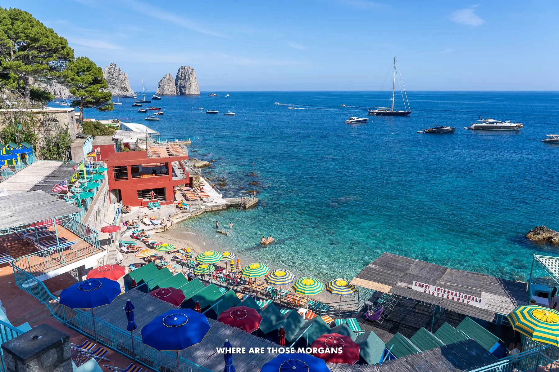 Photo of a small beach area with sun loungers and people bathing in a small cove in Capri